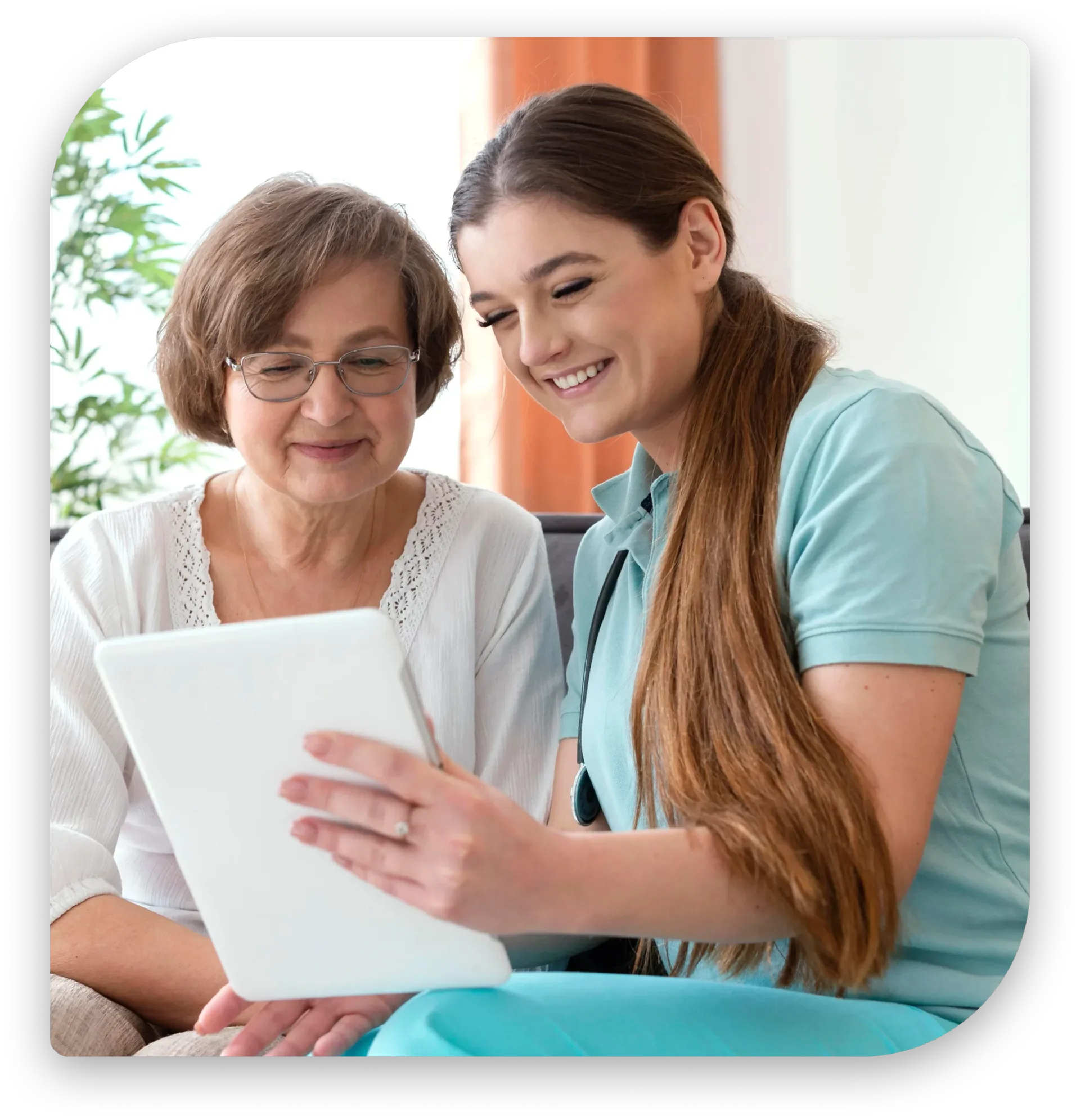 Caregiver in scrubs showing tablet screen to smiling elderly woman