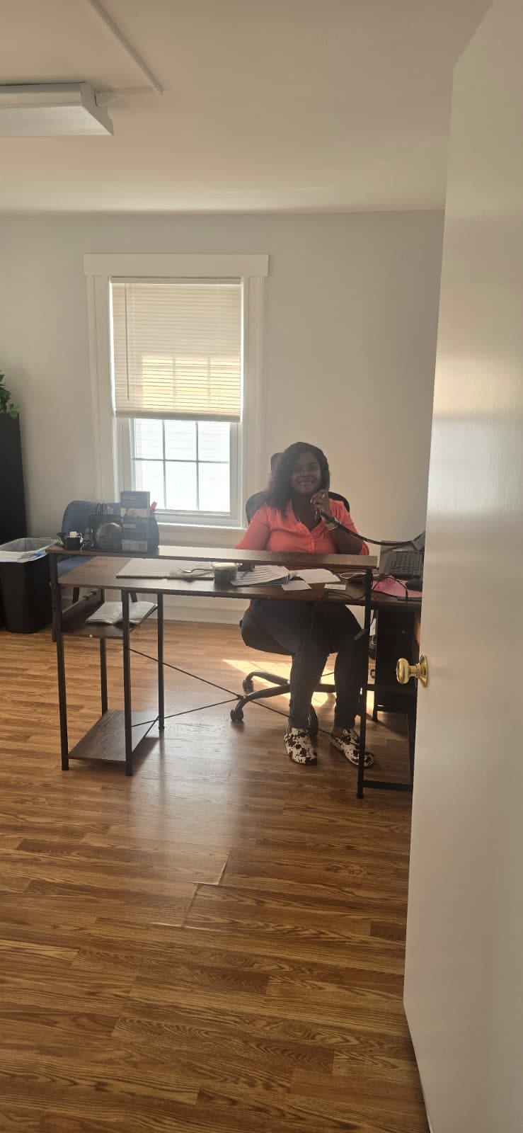 Care coordinator in orange shirt smiling while on phone at office desk